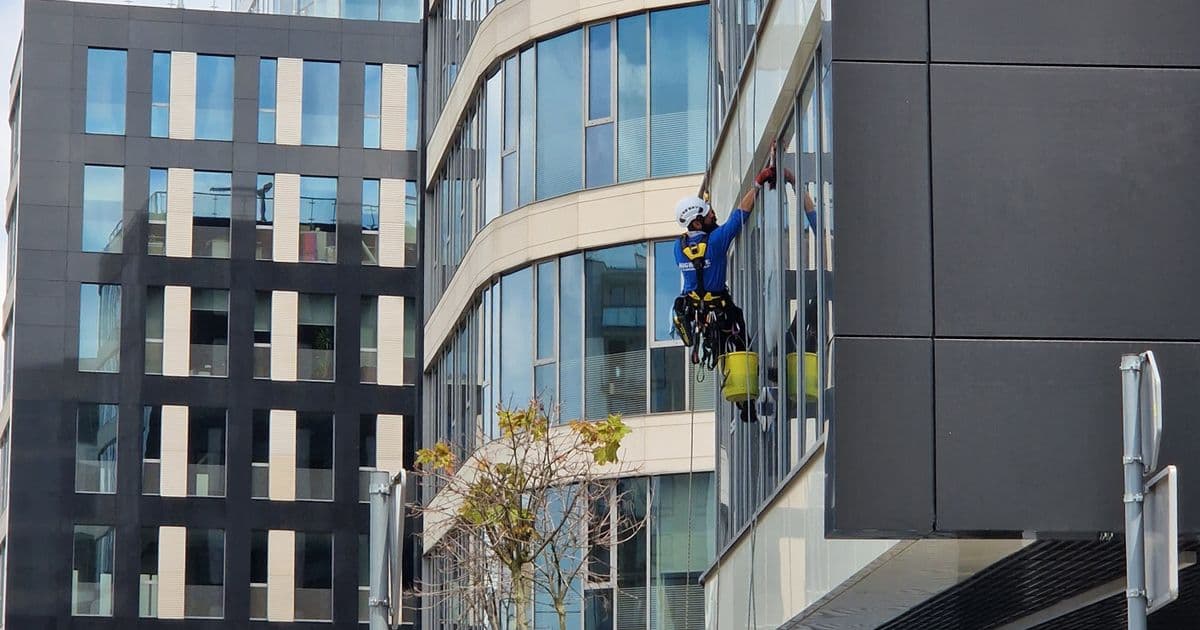 Fassadenreiniger arbeitet mit Seilzugangstechnik an der Glasfassade eines Bürogebäudes – Lohngruppe 6 Gebäudereinigung