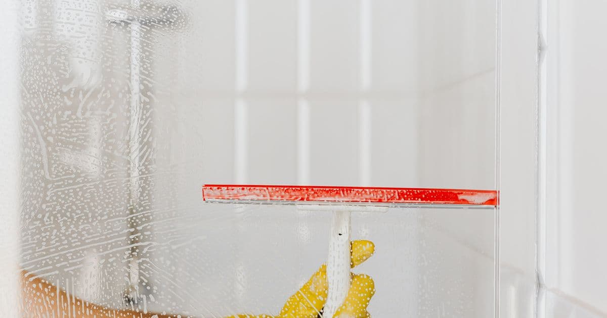 Reinigungskraft reinigt mit rotem Abzieher eine Glasfläche – Glasreinigung wird nach Glasfläche pro m² abgerechnet